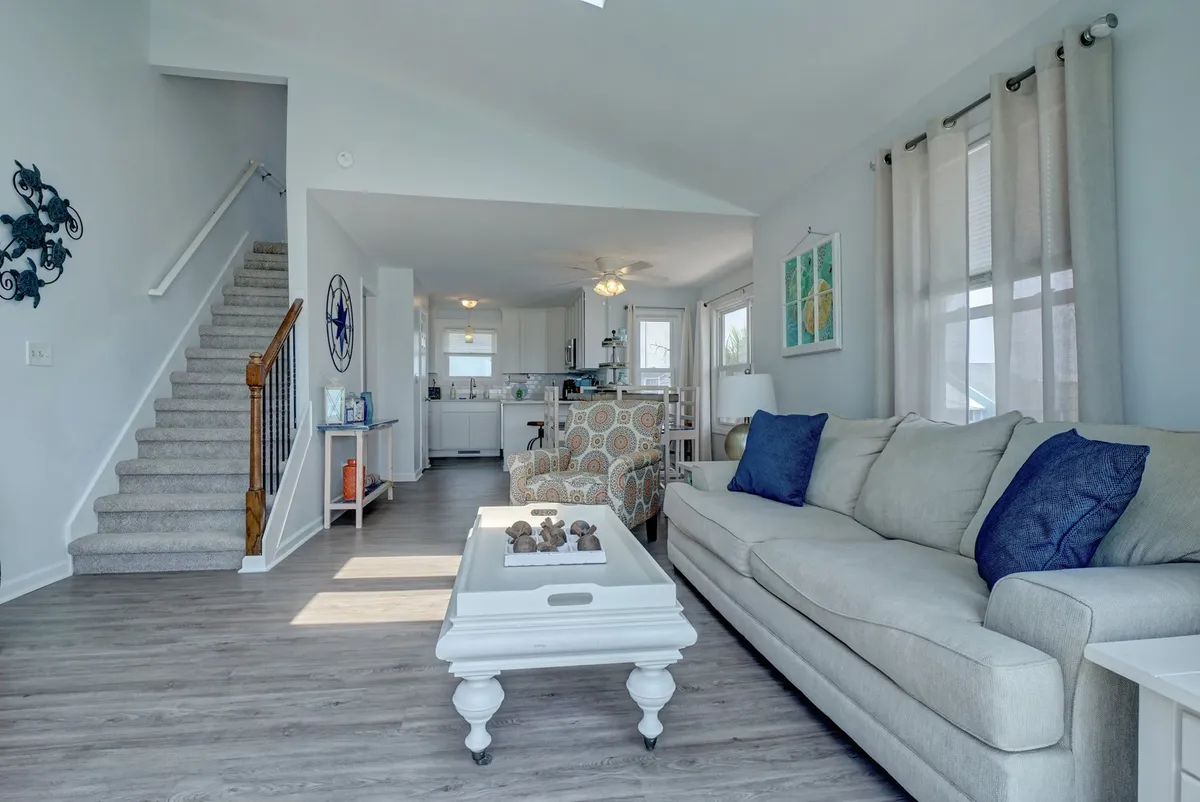 A bright and comfortable main living area with a sofa, coffee table, a staircase, and visible kitchen area. The easy-to-clean flooring and open design are apparent, making it a practical and relaxing gathering space for all family members, pets included.