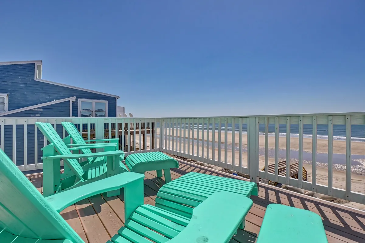 This exterior image features turquoise lounge chairs positioned to gaze at a pristine beach and gentle ocean waves. The relaxed, tranquil mood is enhanced by the proximity to the water, with the lounge chairs providing inviting, comfortable seating perfect for people and pets alike, and immediate access to sandy adventures.