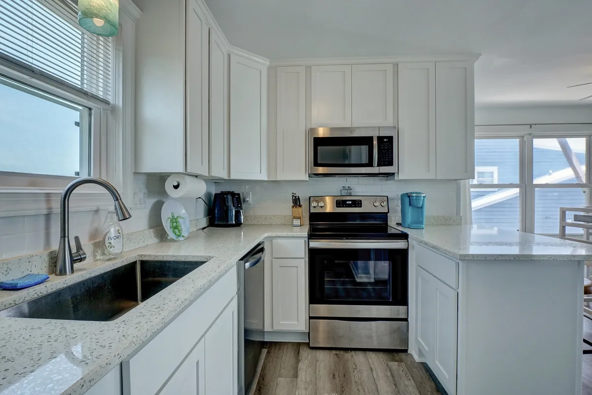 A bright, cheerful kitchen with a central island, stainless steel appliances, and a window bathing the room in daylight. The space is functional yet inviting, emphasizing ease of cooking and entertaining at home.